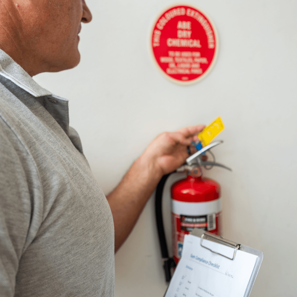 FitSafe Inspector inspecting a fire extinguisher with a safety sign on the wall.