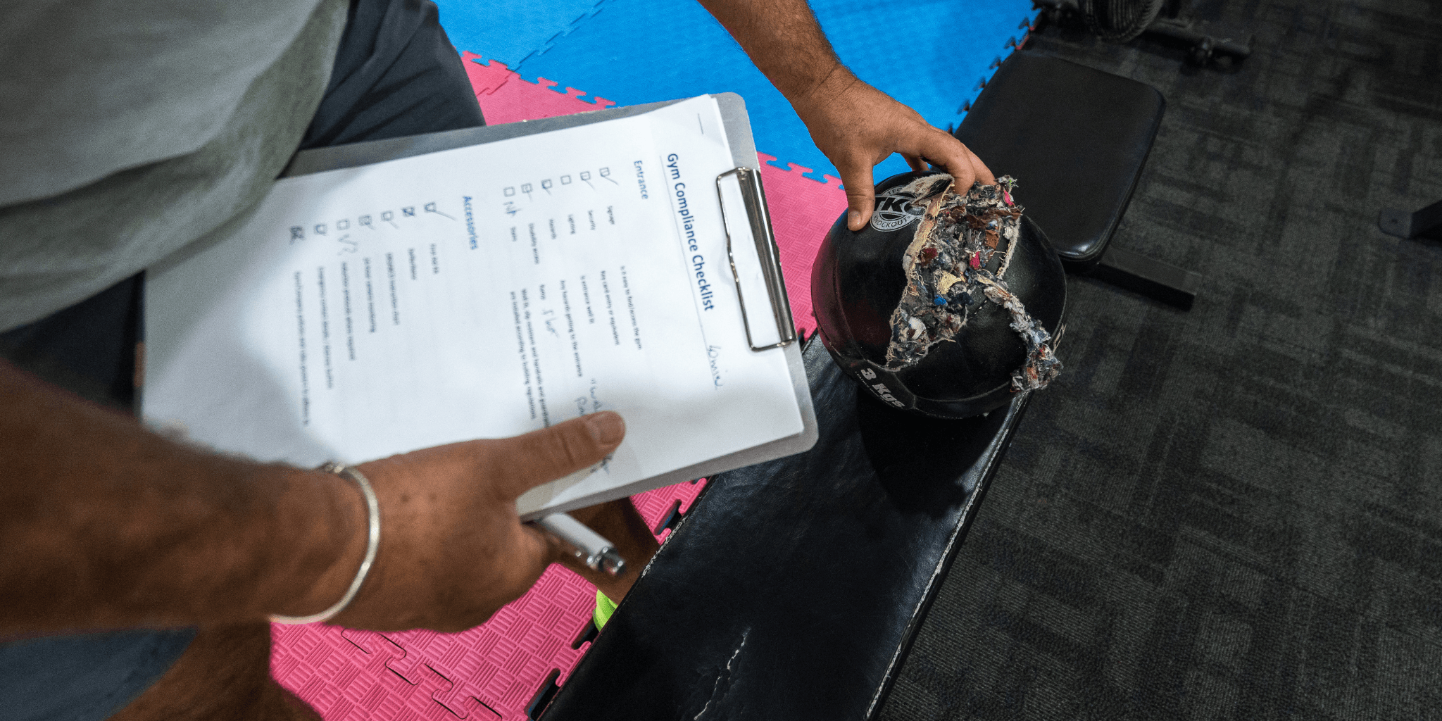 FitSafe Inspector holding a clipboard with a form on a black chair with a pink cushion.